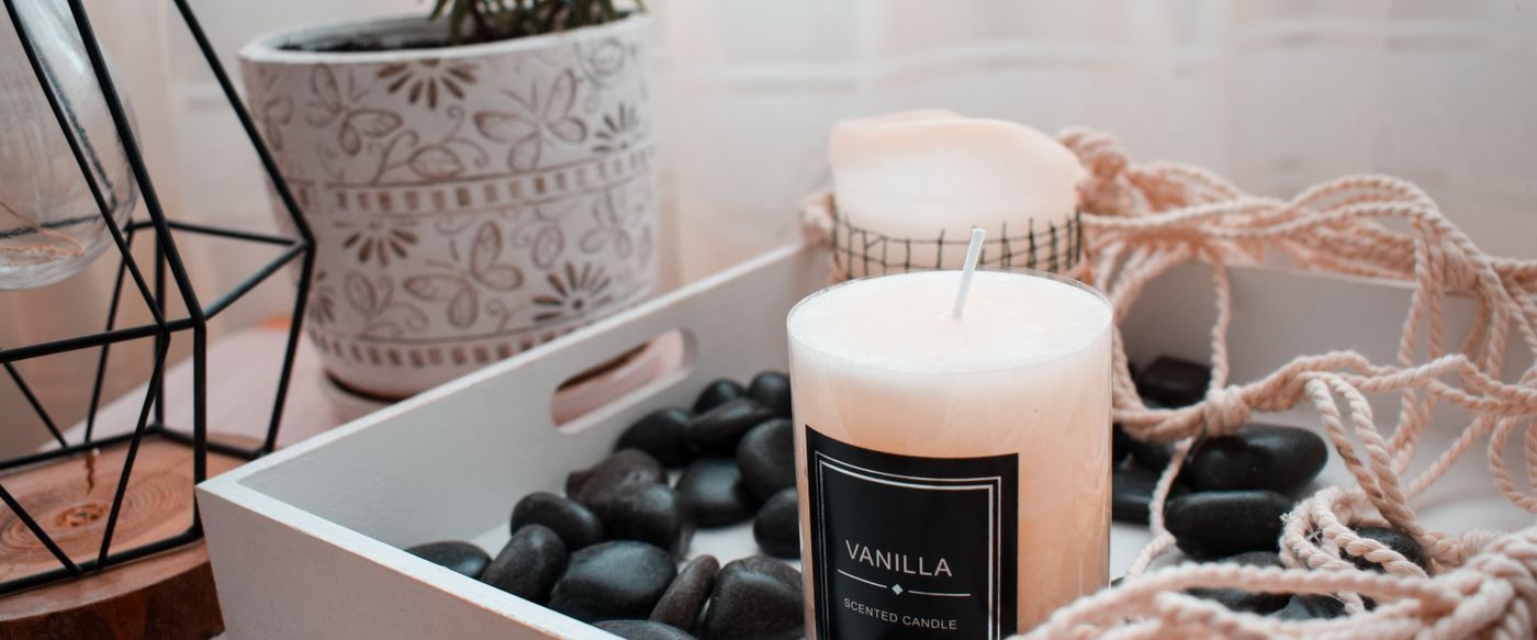 A vanilla scented candle glowing on a wooden tray in a softly lit living room