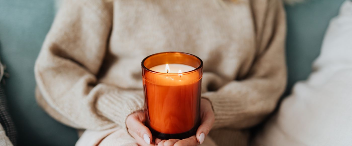 A woman holding a lit candle in a cosy room, choosing home fragrance by weight